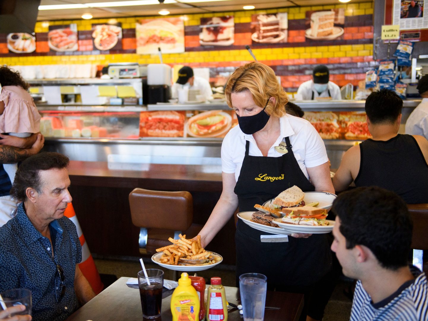 A server delivers food to customers dining at a restaurant in Los Angeles on Aug. 7. Restaurants are boosting pay to attract workers, and that could have an impact on already-high inflation.