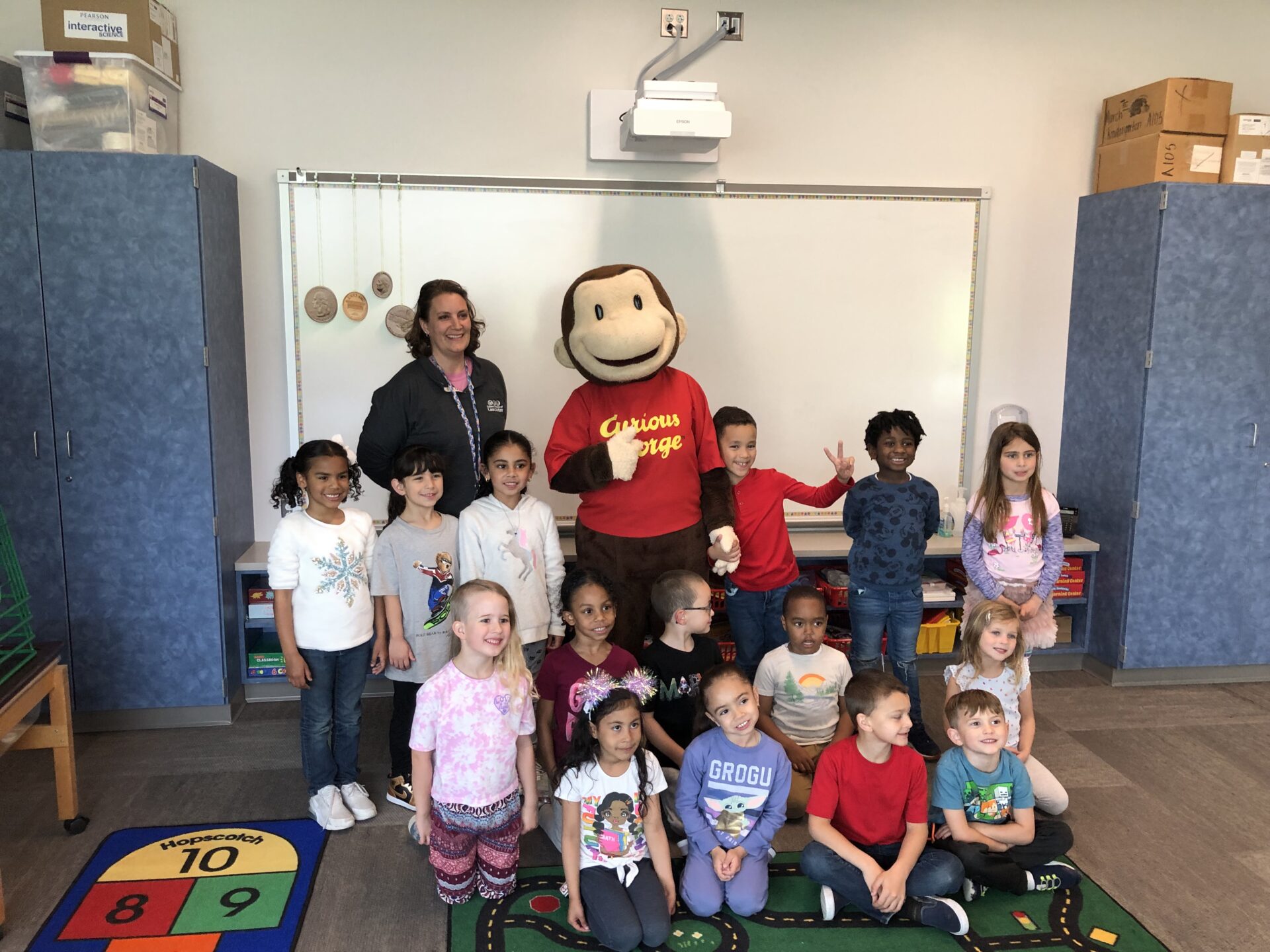 A class and teacher pose with Curious George during an Explore in the Classroom session.